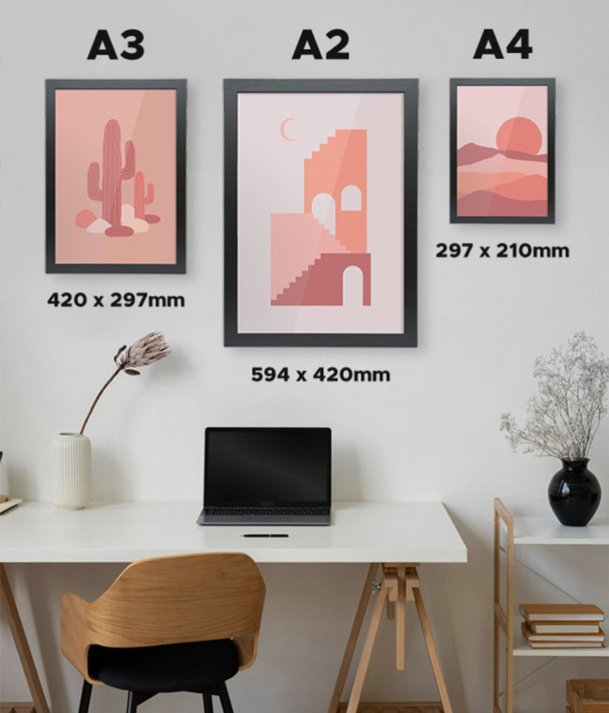Three framed artworks on a wall above a desk with measurements displayed.