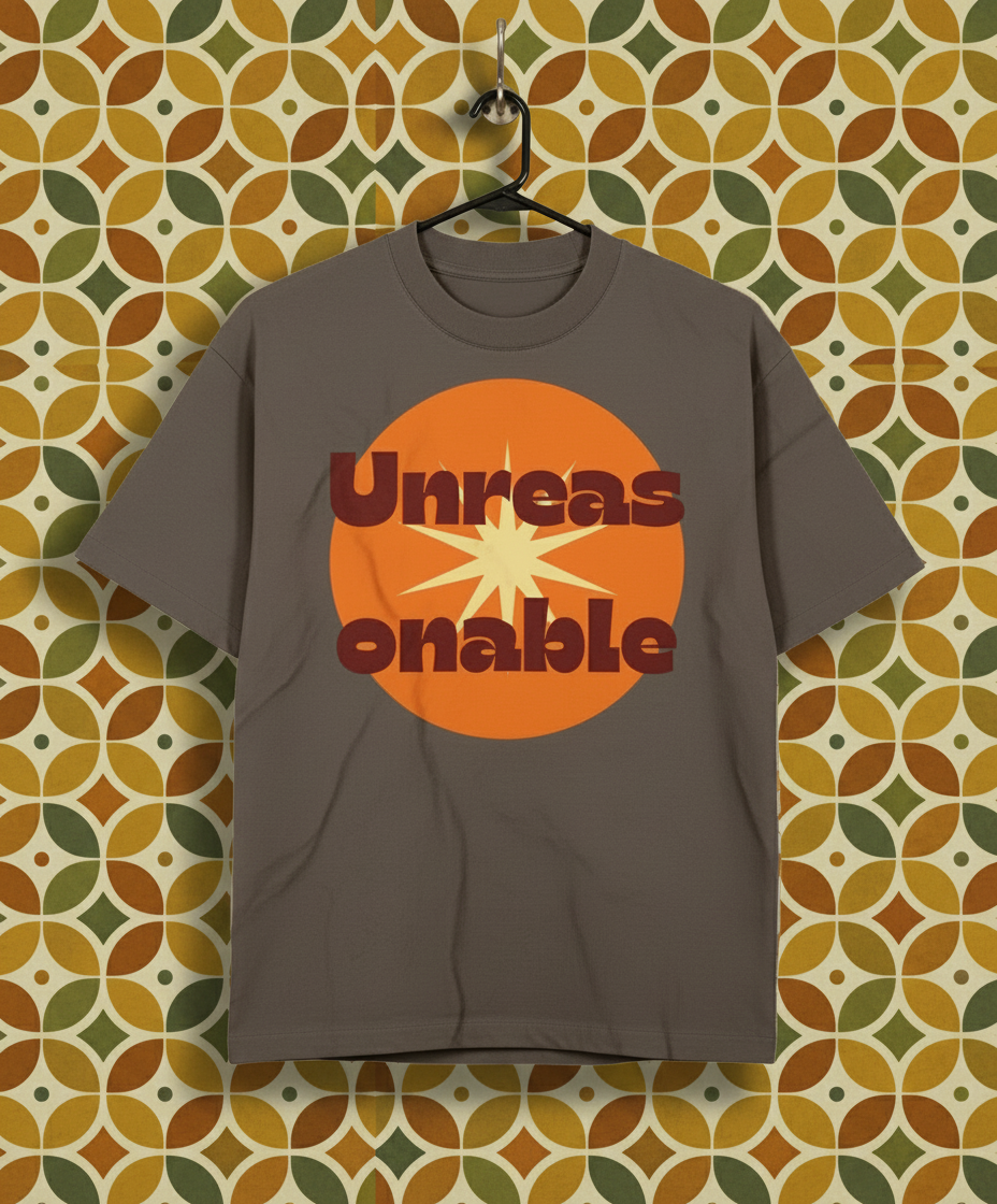 Gray t-shirt with orange and red graphic design on a hanger against a patterned wall.